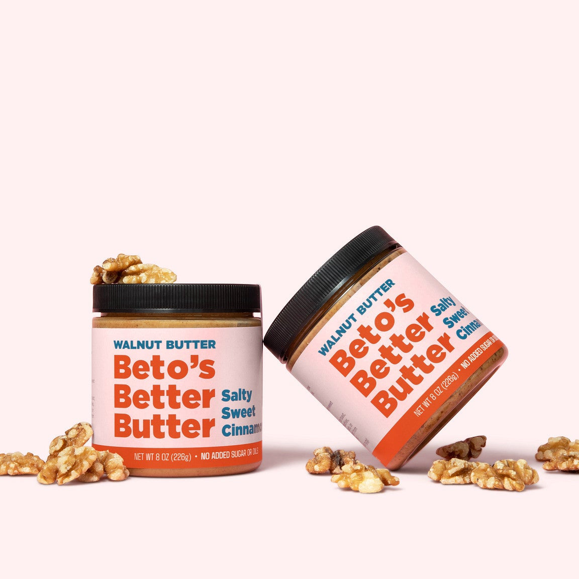 Two jars of Beto's Butter with scattered walnuts on a light pink background