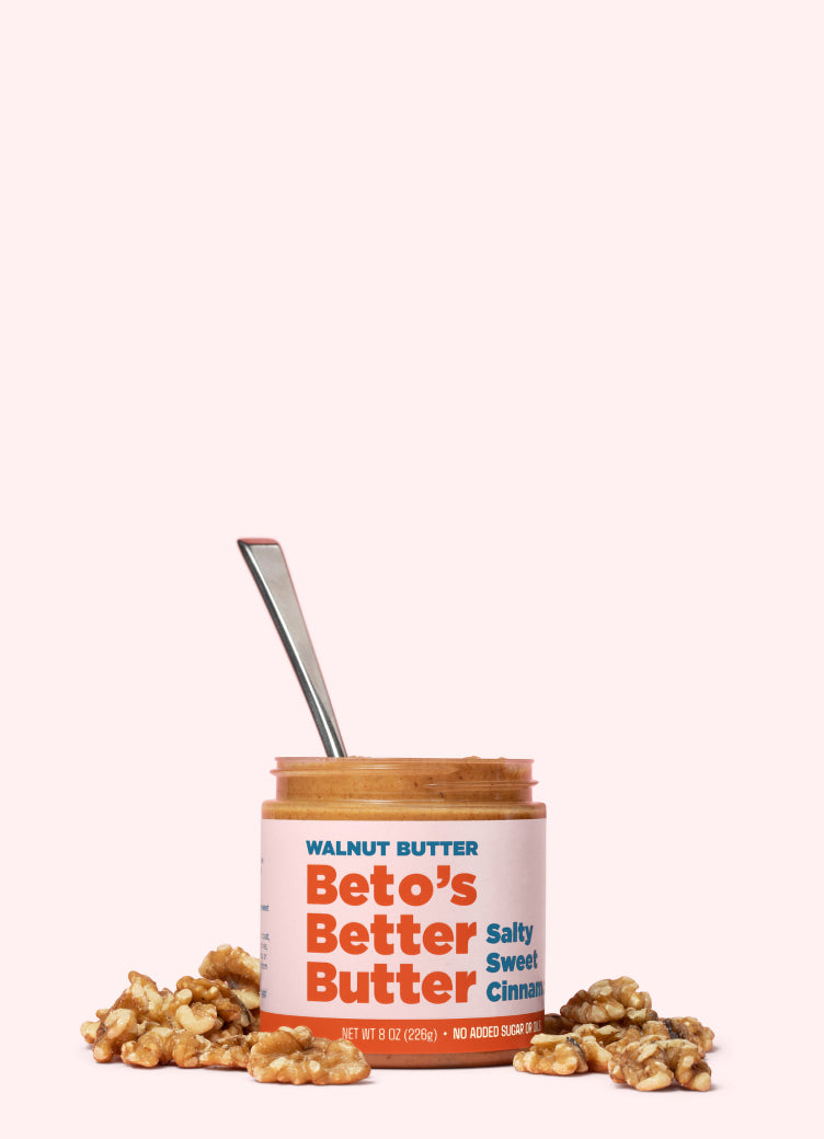 Jar of Beto's Better Butter with a spoon and walnuts on a white background